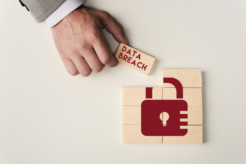 Hand grabbing wooden block with "Data Breach" written on it from a collection of wooden blocks that make up the image of a lock.