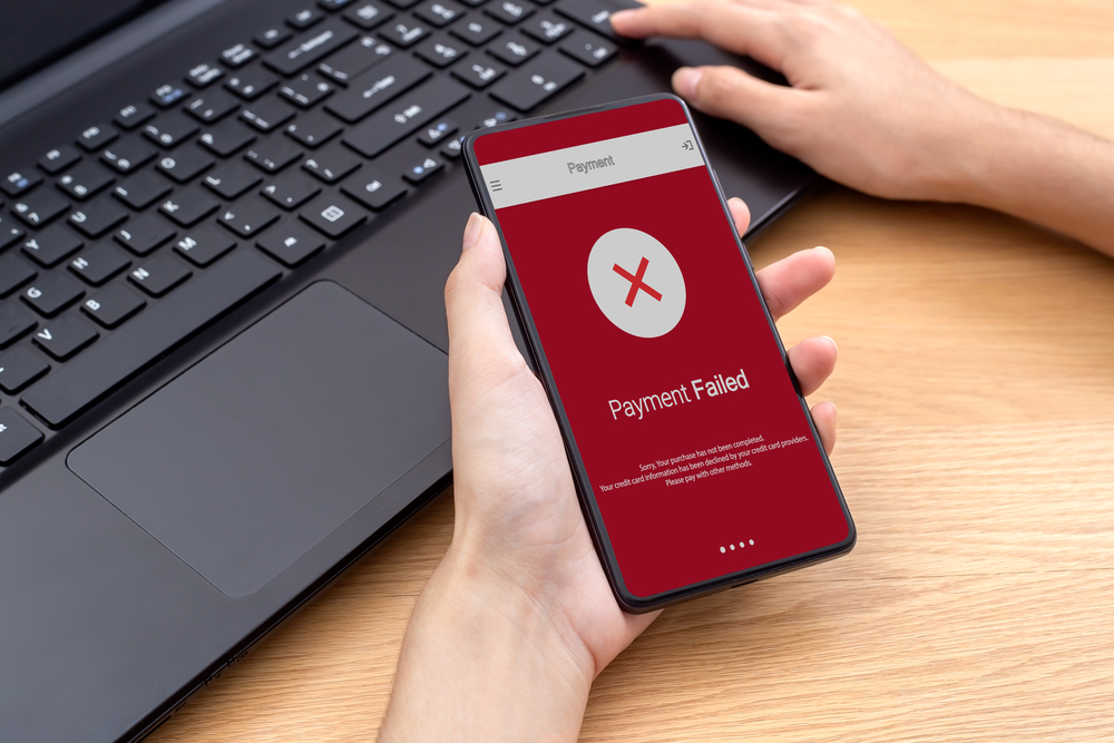 Person holding mobile phone that has a red screen that reads "Payment Failed"