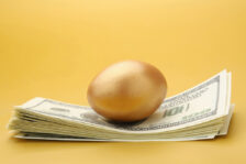 Golden egg on top of large stack of cash.