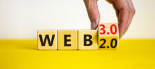 Hand turning over a cube that says "2.0" to a new face that says "3.0" in front of a series of cubes that spell "web".