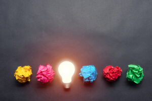 Idea generation, light bulb glowing and surrounded by crumpled notes.