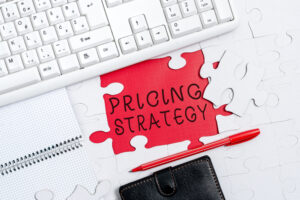 Pricing Strategy puzzle piece in front of a computer keyboard and above a wallet.