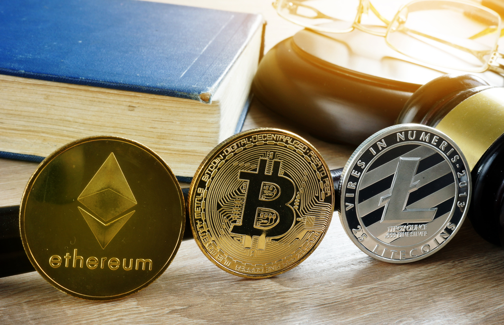 Cryptocurrency coins, Bitcoin, Ethereum, and Litecoin, standing in front of a gavel and book.