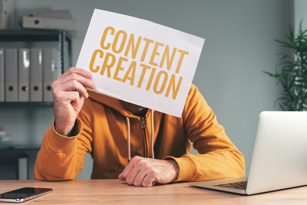 A person in an orange hoodie holding up a sign that says "content creation"