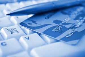 blue photograph of a pen and credit card on top of a computer keyboard with the shopping cart logo