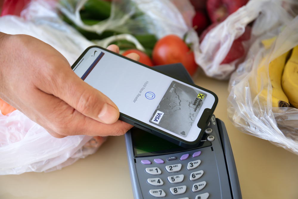 Man hand holding Apple iPhone 13 with Apple Pay on the screen and POS pay pass online terminal. iPhone was created and developed by the Apple inc.