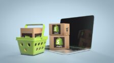 A green shopping basket with a cardboard box inside it next to two cardboard boxes with the Shopify logo on them sitting atop an open laptop computer.