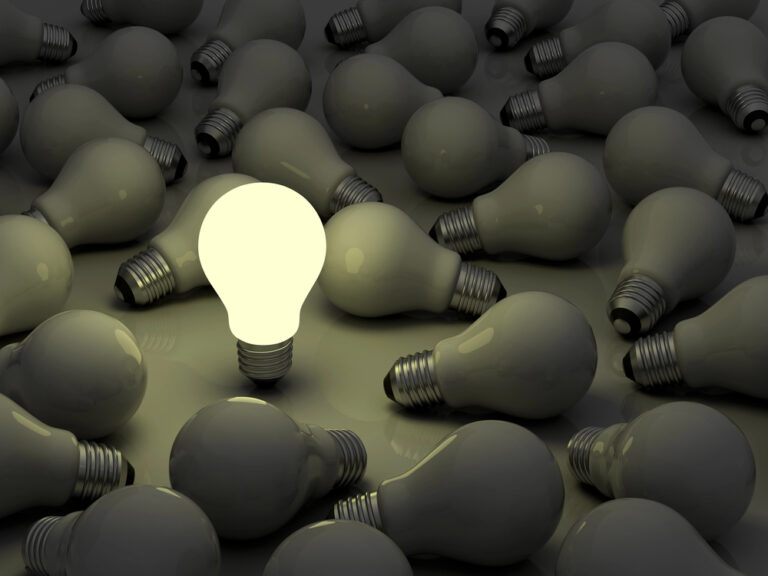One lit lightbulb surrounded by many unlit lightbulbs