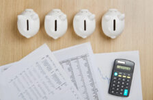 Top-down view of four piggy banks above a stack of papers and calculator on a wooden desk.