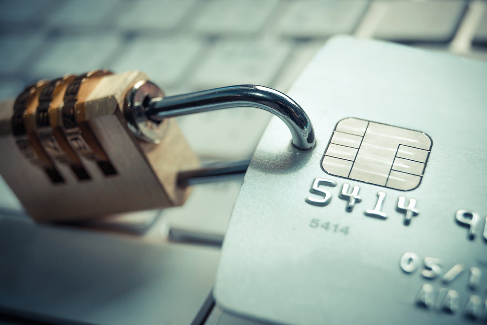 A padlock on the left and a credit card on the right, both atop a laptop keyboard