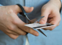 Man cutting a credit card in half with scissors.