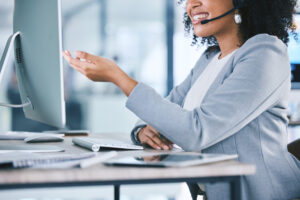 Call center, customer service and a woman talking at computer with microphone. Hand and smile of african person as crm, telemarketing and sales or technical support agent with headset and desktop pc.