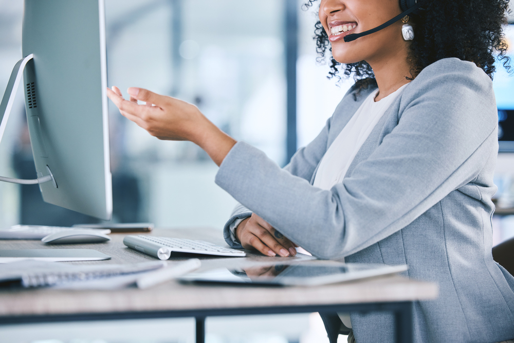 Call center, customer service and a woman talking at computer with microphone. Hand and smile of african person as crm, telemarketing and sales or technical support agent with headset and desktop pc.