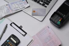 A desk showing a credit card, laptop, calculator, credit card reader, and files