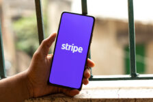 Hand holding a mobile phone with a "Stripe" logo in front of a blurry outdoor background