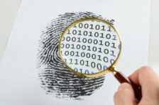 Magnifying glass displaying binary code while zooming into a large fingerprint printed on a large piece of paper