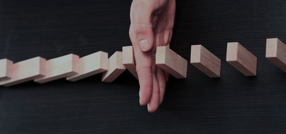 Male hand stopping a series of wooden blocks from continuing to fall in a domino effect, planning and strategy