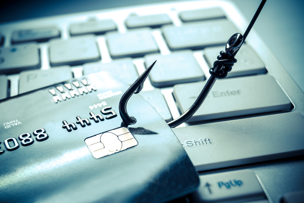 A fishing hook through a credit card on top of laptop keyboard, phishing, credit card fraud, payment fraud