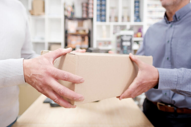 One person handing a cardboard box over a counter to another person.