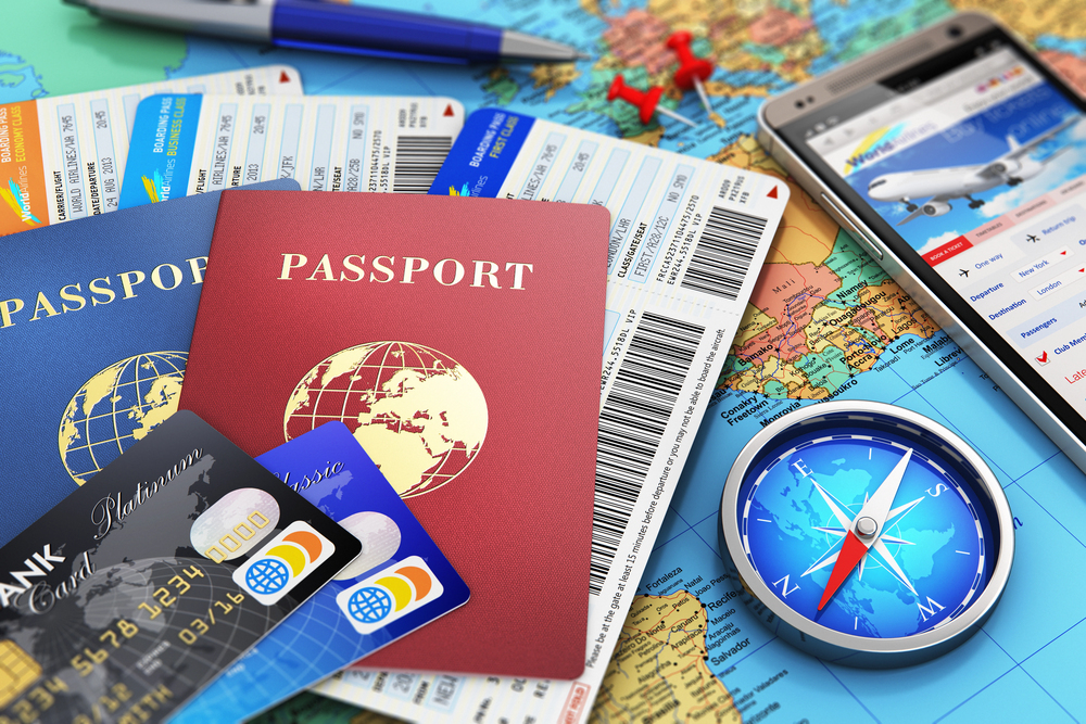 Creative abstract business travel and tourism concept: air tickets or boarding pass, passports, touchscreen smartphone with online airline tickets booking or reservation internet application, magnetic compass, credit cards and pen on world geographic map atlas with selective focus effect